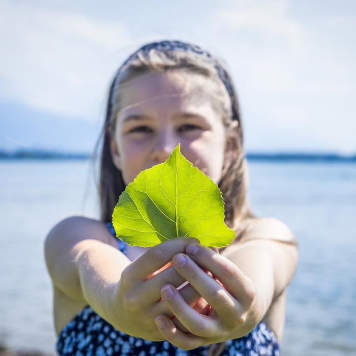 Ein Mädchen hält ein Blatt in Richtung Kamera, um Nachhaltigkeit und Naturschutz zu symbolisieren. 